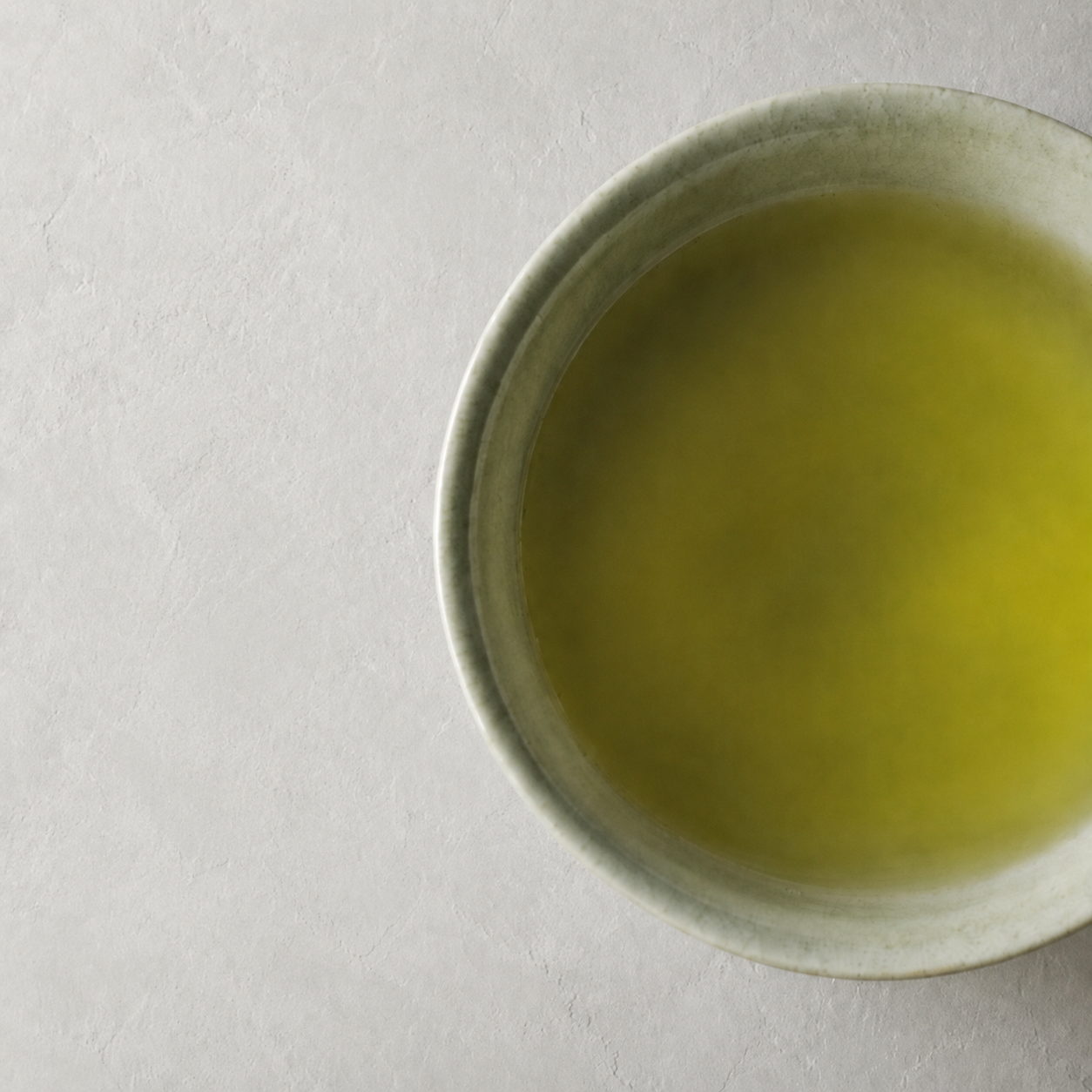 白い壁の静かな余白と、淡い緑色の煎茶を満たした陶器の茶碗
